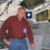 Jeff Hoff standing behind flight deck. Windows behind Jeff are looking into the cargo bay of the shuttle orbiter.